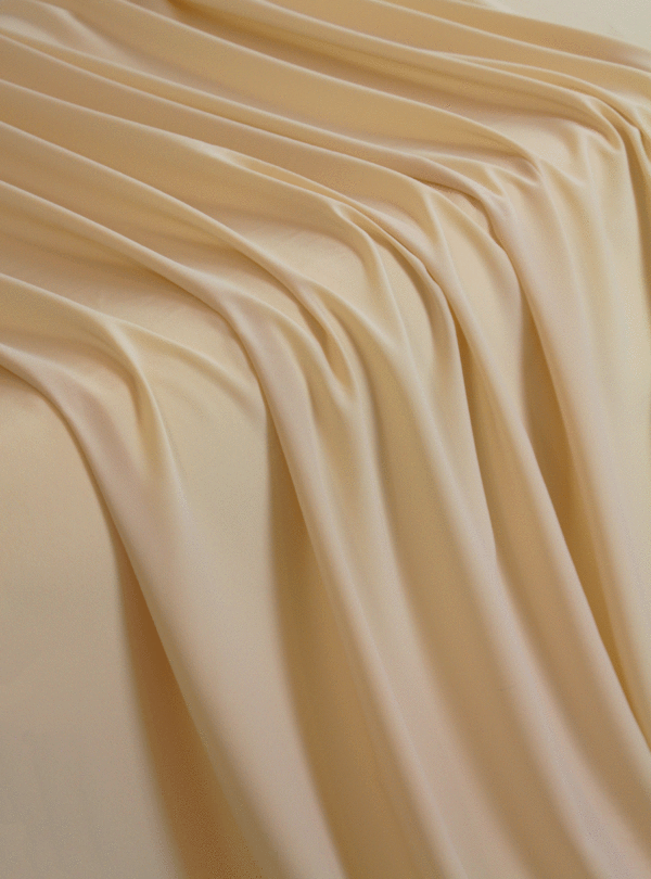 A solid ivory crepe wool dobby fabric flowing over a table in a waterfall pattern.