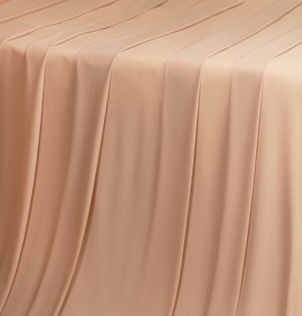 A solid light peach-mauve georgette fabric flowing over a table in a waterfall pattern.